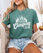 Person wearing a green t-shirt with 'Camping Crew' design, sitting indoors.