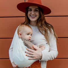 Woman holding a baby in a sling against an orange wall