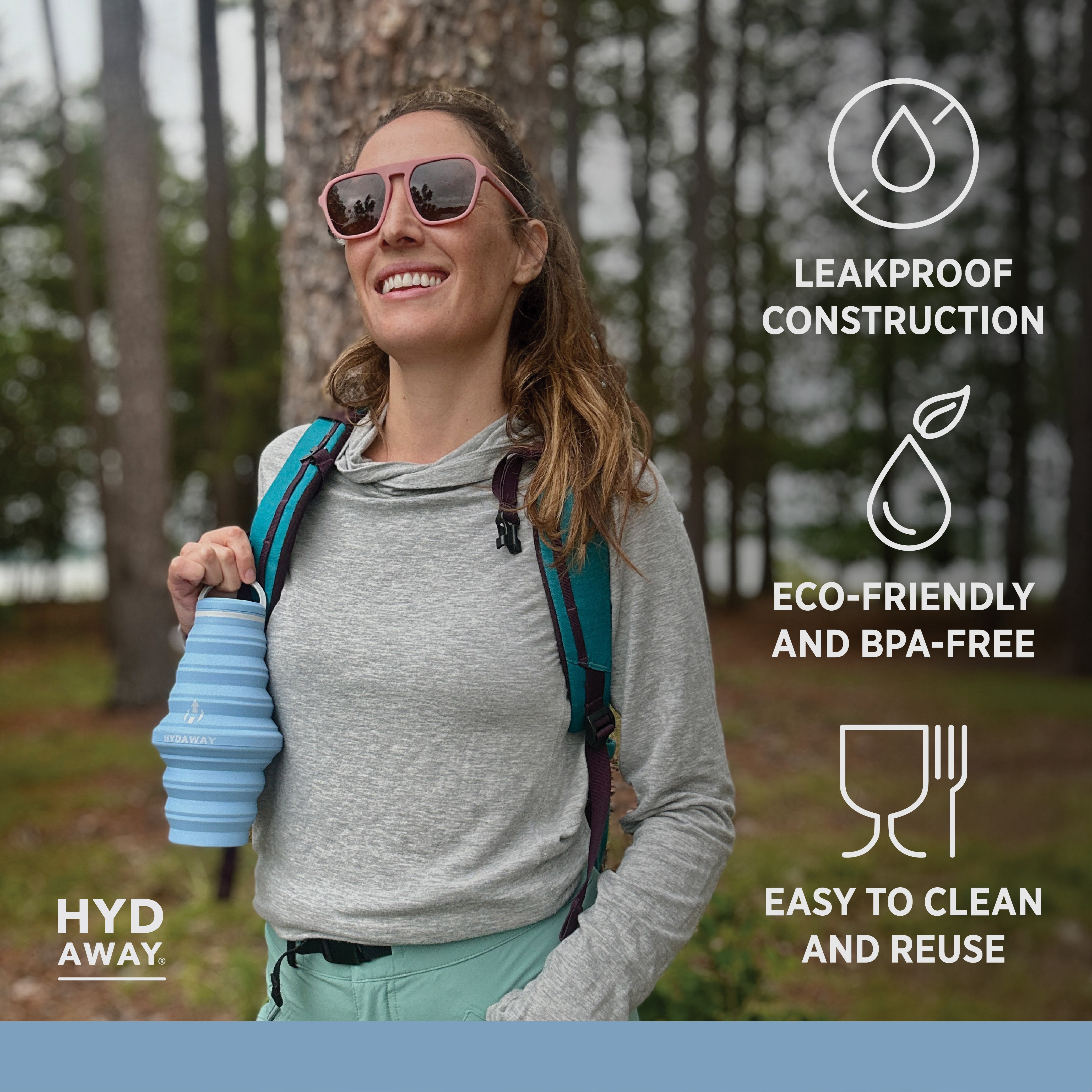 Woman outdoors holding a blue water bottle with 'Hyd Away' branding, surrounded by nature.