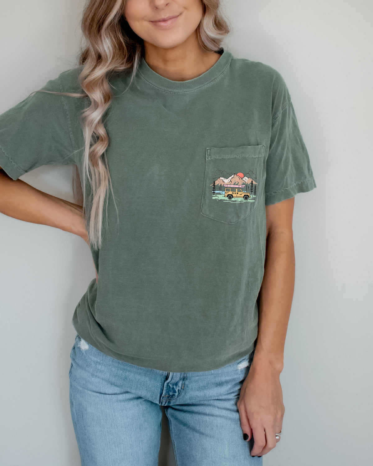 Person wearing a green t-shirt with a pocket design against a plain background