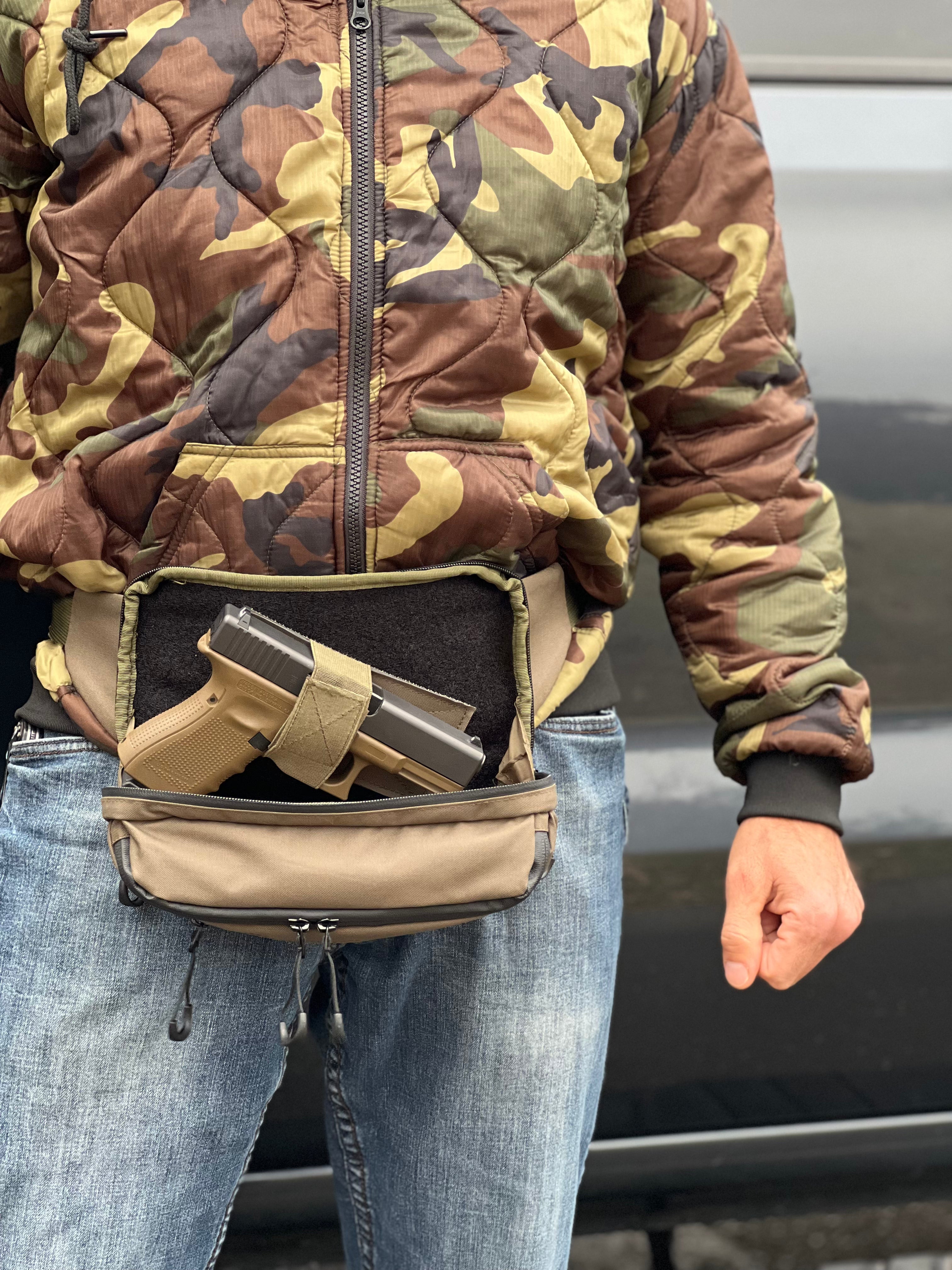 Person wearing a camouflage jacket with a waist bag containing a gun and ammunition.