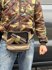 Person wearing a camouflage jacket with a waist bag containing a gun and ammunition.