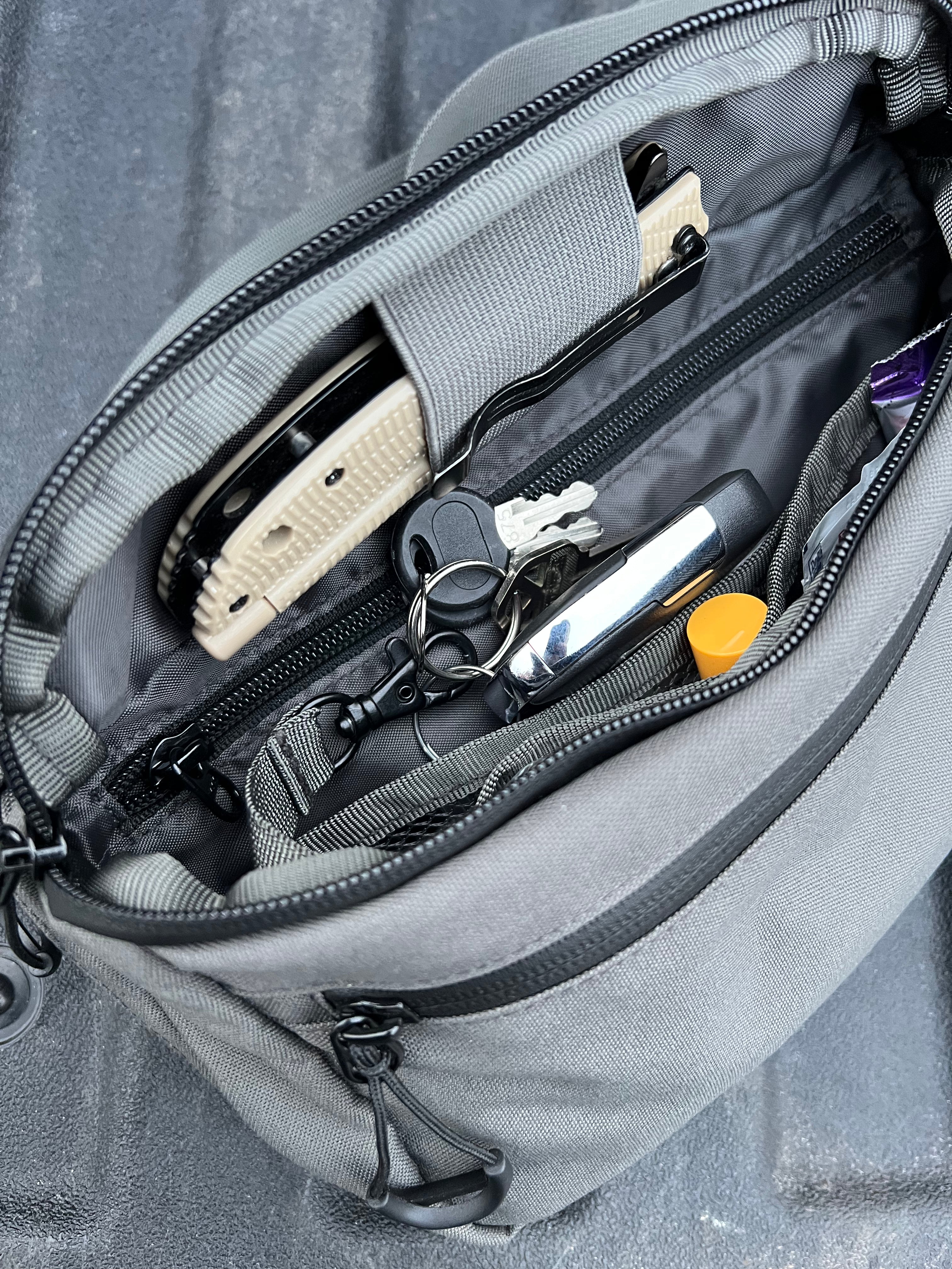 Gray backpack with items like a knife, keys, and a pen inside