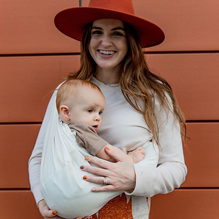 Woman holding a baby in a sling against an orange wall