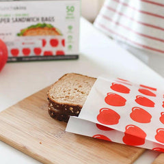 Loaf of bread on a cutting board with a package of red-patterned sandwich bags in the background.