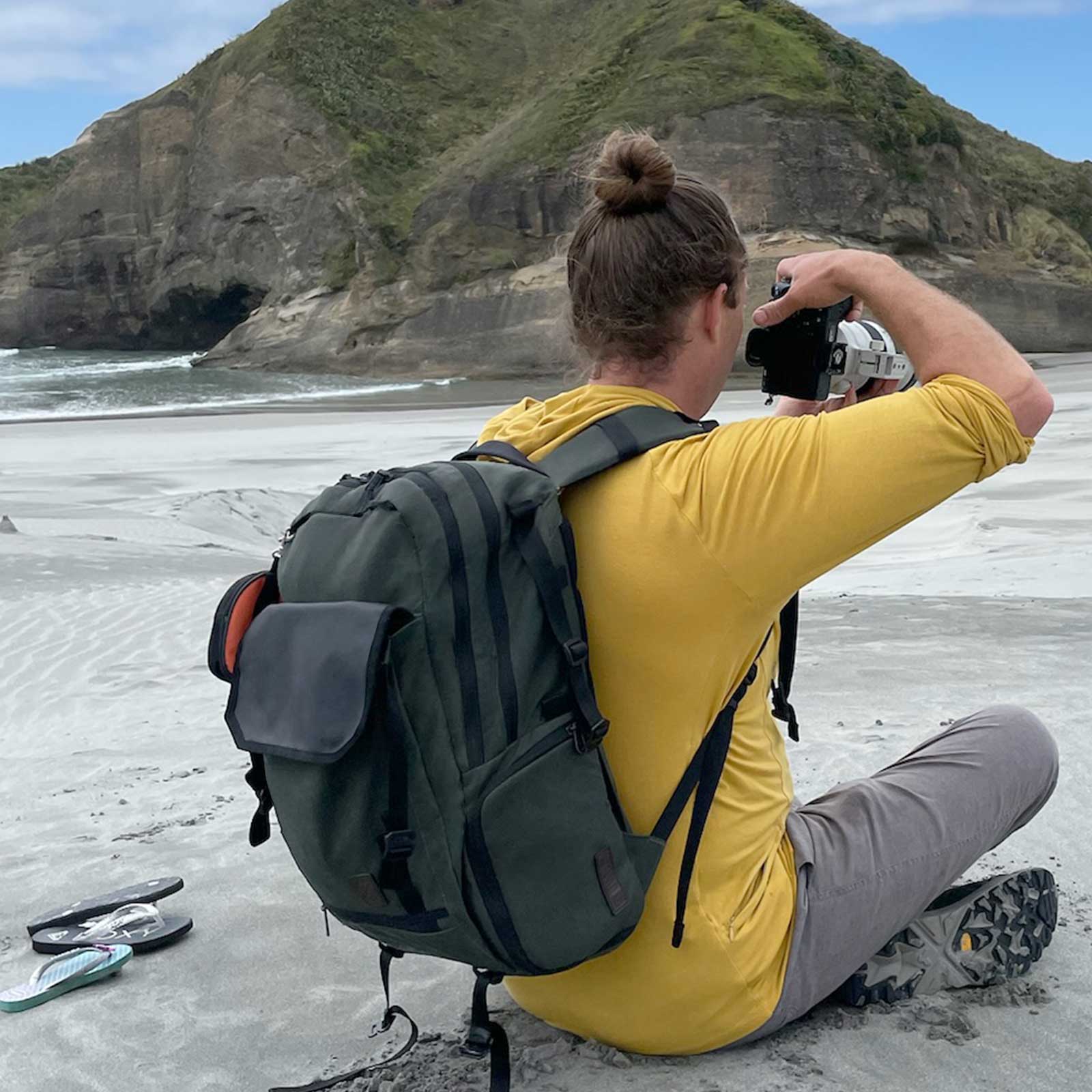 Person taking a photo on a beach with a mountain in the background