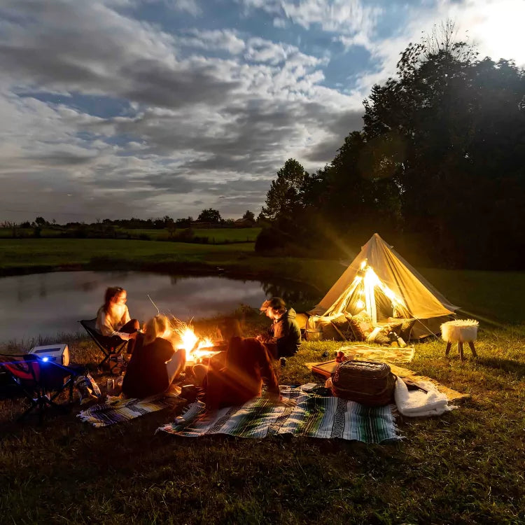 People camping by a lake with a tent and fire pit, surrounded by nature.